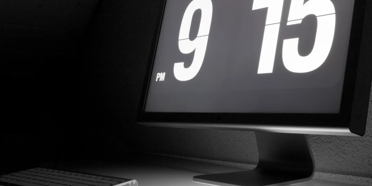 Schwarzweißaufnahme eines Monitors, der in sehr großen Ziffern die Uhrzeit 9:15 anzeigt, davor der Rand einer Tastatur